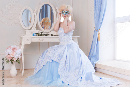 A beautiful, young blonde woman sits by the dressing table and wore a blue mask dressed in a ball gown, going to the carnival. Princess in the Versailles, France. photo