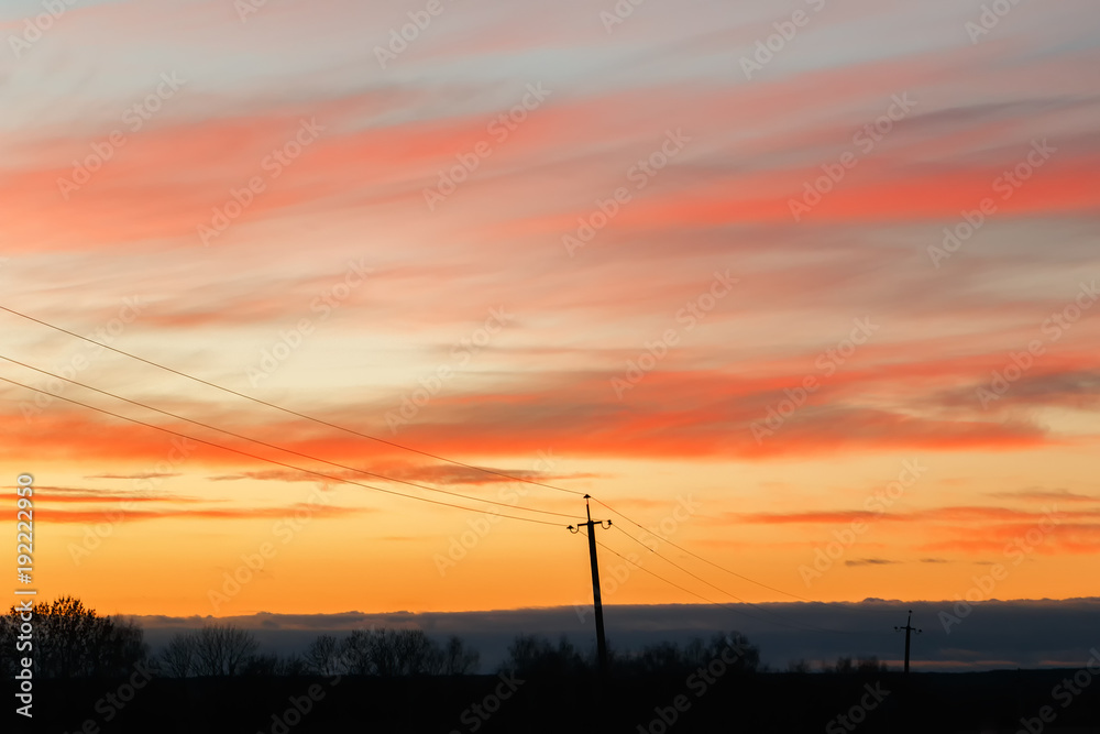 Silhouette of high voltage power lines against the background of dramatic sky at sunset.