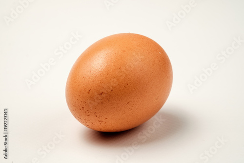 Single brown chicken egg on a white surface.