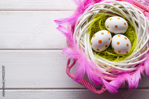 Easter eggs in the nest and pink basket on white wooden table