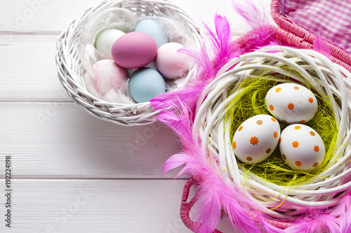 White and colored Easter eggs in basket on white wooden background