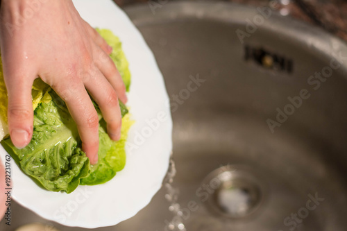 girl hands cleaning lettuce with the water of a kitchen tap, lettuce in a plat
