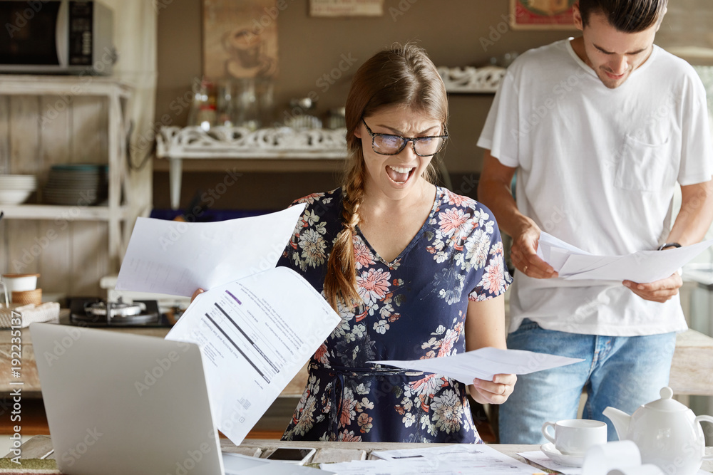 Obraz premium Frustrated female tries to make decision about mortgage, consider investments, work at kitchen. Annoyed woman looks at unpaid domestic bills with displeased expression, checks documentation.