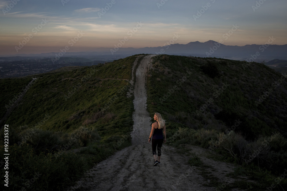 Rear view of woman walking on mountain trail during sunset Rear view of woman walking on mountain trail during sunset