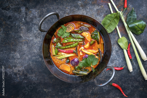 Traditional Thai kaeng phet red curry with vegetables as top view in a wok with copy space left