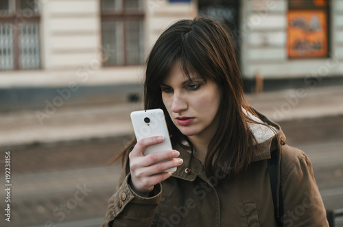 Young brunette girl walking and texting on the smart phone in the street