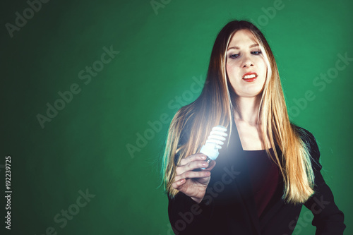 Serious young business woman holding a light bulb on a green background. © Pavel