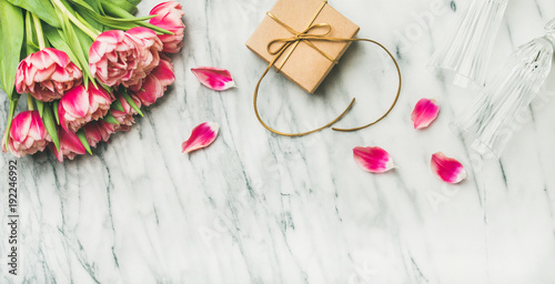Valentines day holiday background. Flat-lay of pink tulips bouquet, champaign glasses and gift box with ribbon over white marble table, top view, copy space. Lovers or Womens day greeting card photo