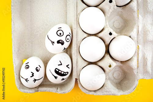Easter eggs with drawn cartoon faces in tray on yellow background.