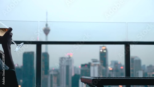 Happy woman drinking a glass of white wine while sitting in rooft bar in the city or on the terrace with cityscape at sunset. Vacation,happiness,freedom concept. photo