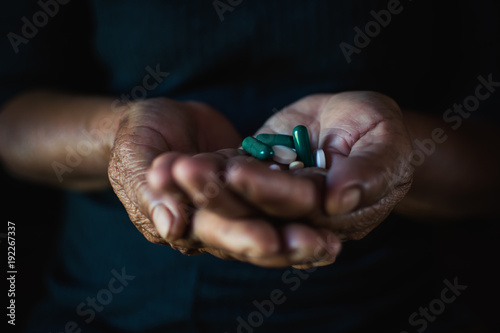 Close up hand of old woman holding a pill on black background, concept illness and healthcare