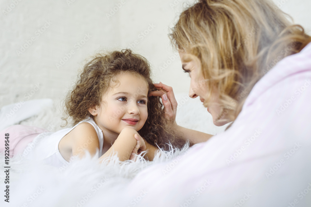 happy mother and adorable curly daughter lying on sheep skin blanket happy mother and adorable curly daughter lying on sheep skin blanket