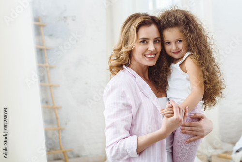 beautiful happy mother holding on arms her smiling curly daughter