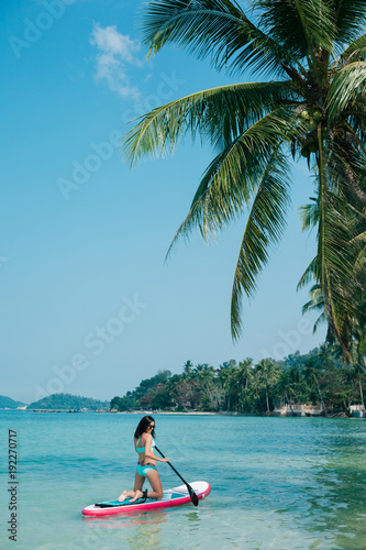 girl on stand up paddle board on sea at tropical resort