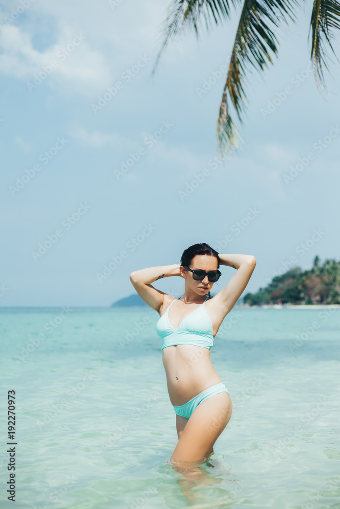 young woman in bikini and sunglasses at tropical sea resort