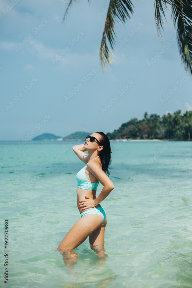 slim girl in bikini and sunglasses at tropical sea resort