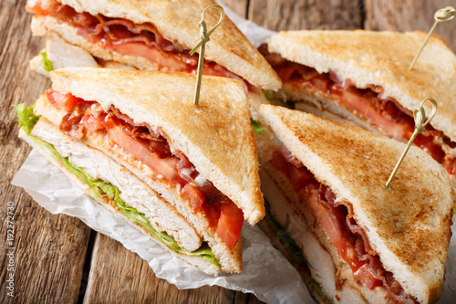 Hearty club sandwiches with meat turkey, bacon, tomato and lettuce close-up on paper. horizontal