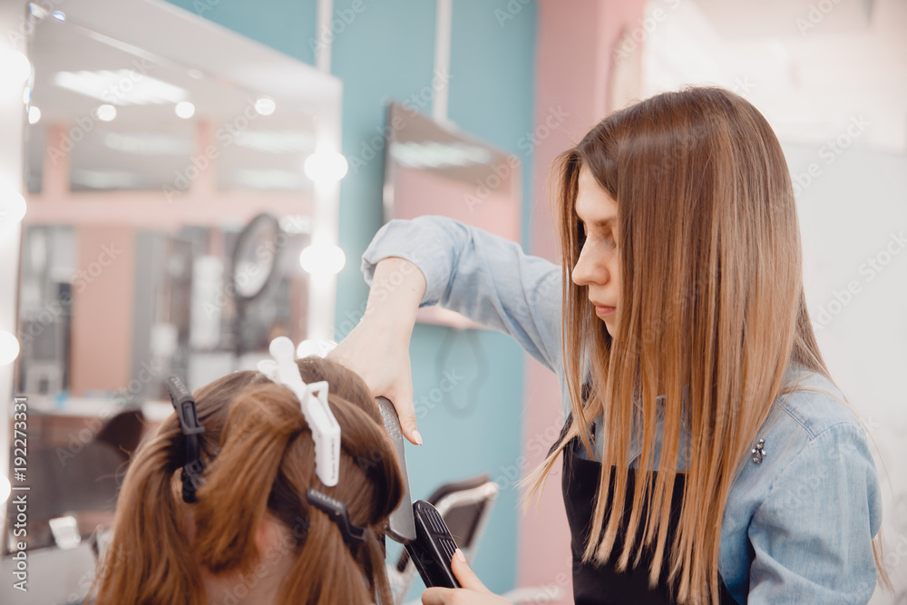 Close up of hands of professional hairdresser beauty salon, straighteners curling female hair Close up of hands of professional hairdresser beauty salon, straighteners curling female hair