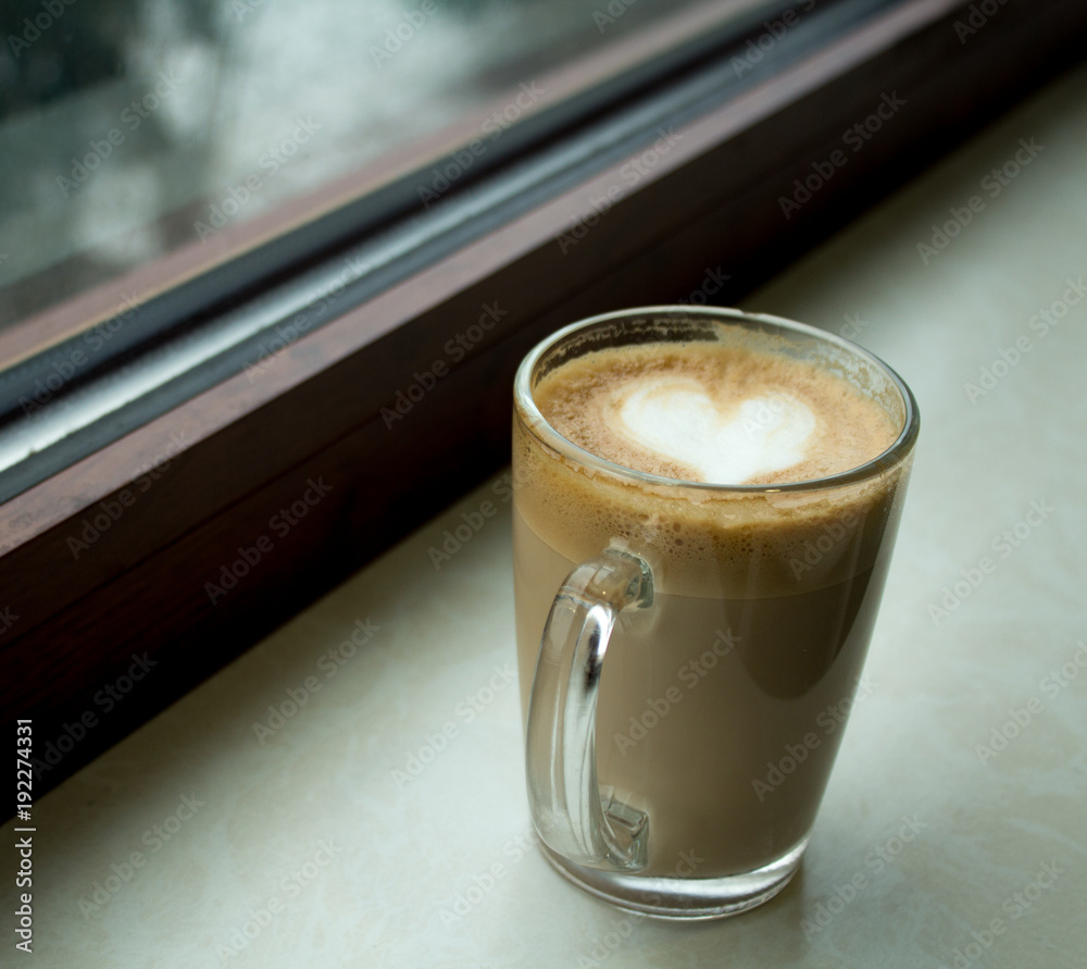 a cup of coffee with a heart of foam near the window a cup of coffee with a heart of foam near the window