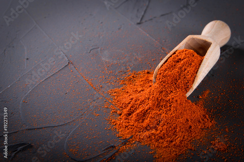 Fotografija Red paprika in a wooden spoon on a concrete stone background