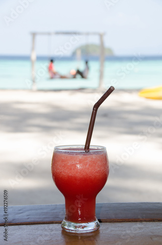 watermelon smoothie on wooden table with happy couple on swing background. Lipe island,Thailand