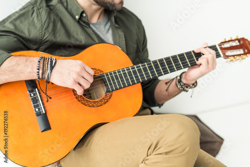 cropped image of man sitting and playing acoustic guitar