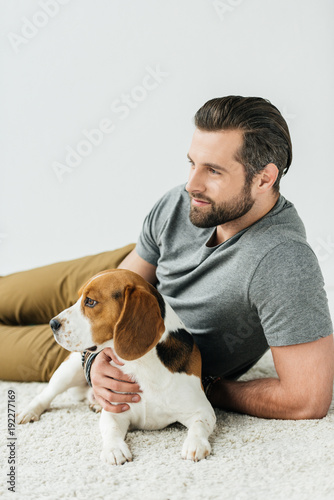 handsome man lying with cute beagle on carpet and looking away