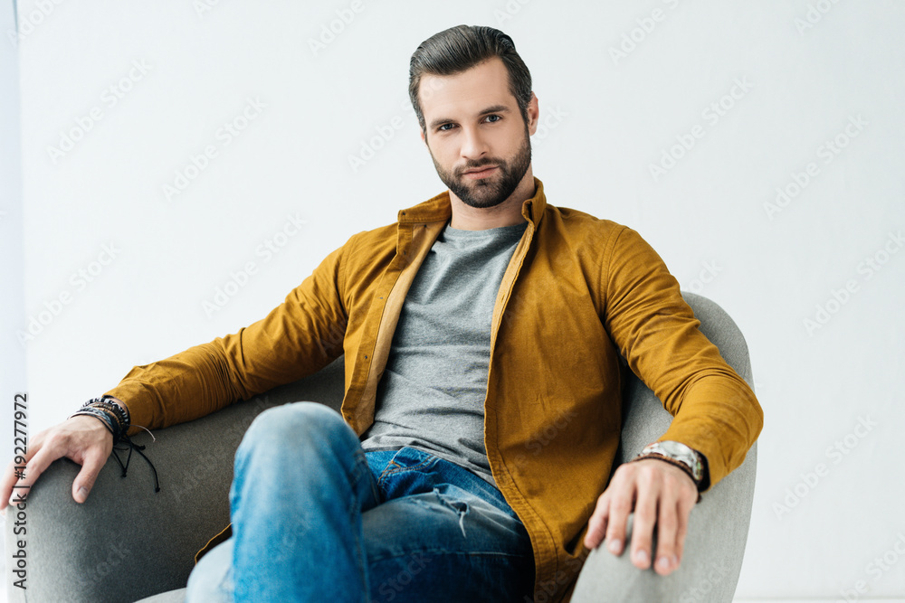 handsome man sitting in armchair and looking at camera handsome man sitting in armchair and looking at camera