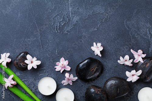 Spa background with massage pebble, green leaves, beautiful flowers and candles on black stone table top view. Aromatherapy, relaxation and zen like concept.