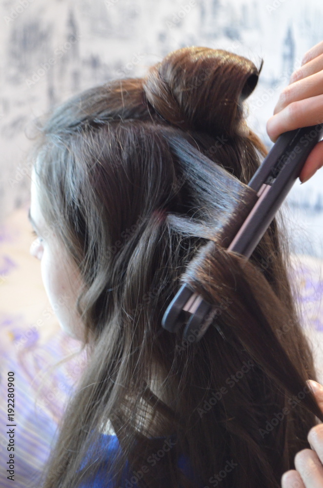 Fototapeta premium Процесс накручивания волос утюжком - красивая молодая девушка с очень длинными волосами 