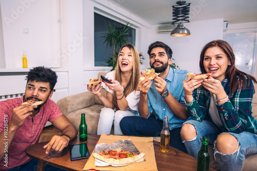 Group of young friends eating pizza and watching tv.Home party.Fast food concept.