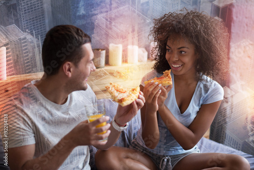 Tasty meal. Joyful happy young couple holding slices of pizza and eating them while looking at each other