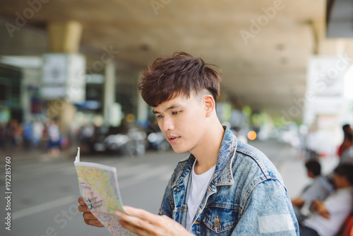 Asian male tourist reading map while waiting for taxi at the airport