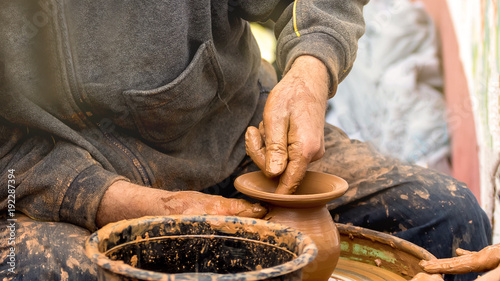 Potter's hands creating a clay vase on a circle.
