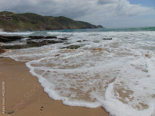 espuma de mar blanca llegando a la arena dorada de playa desierta con montañas y cielo