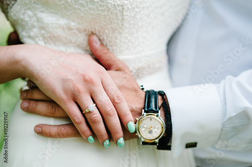 The bride s hand lies on the groom s hand. Shows a gold engagement ring. Wedding ring. Stylish manicure. Close up. Clock on a man s hand.