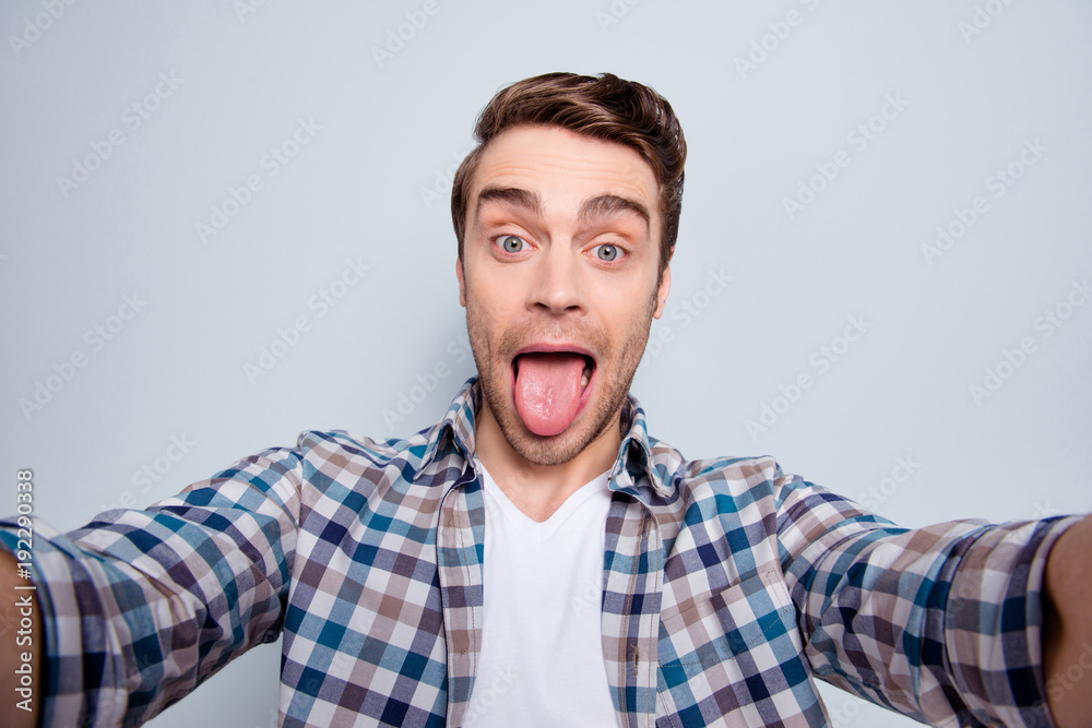 Self portrait of bearded, cheerful, stylish, cool guy in casual outfit, checkered shirt showing tongue-out to the camera over grey background Self portrait of bearded, cheerful, stylish, cool guy in casual outfit, checkered shirt showing tongue-out to the camera over grey background