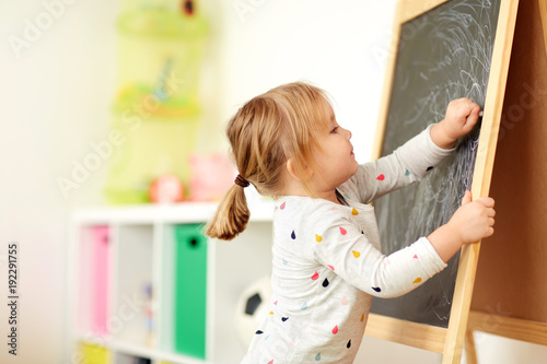 happy little girl drawing on chalk board at home