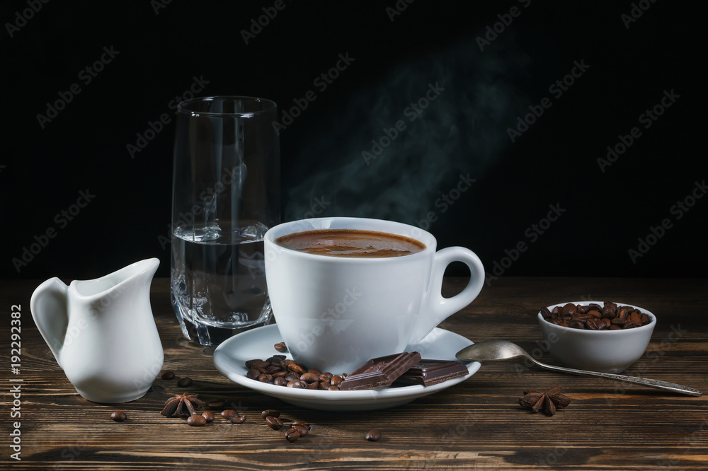 .A cup of hot coffee with cinnamon, chocolate and a glass of cold water on a rustic wooden table on a dark background. Low key. .A cup of hot coffee with cinnamon, chocolate and a glass of cold water on a rustic wooden table on a dark background. Low key.