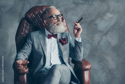 Portrait of posh chic classy virile dreamy trendy dreaming groomed brutal big company chief millionaire sitting on leather armchair smoking cigarette drinking beverage isolated on grey background
