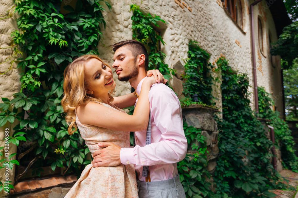 A closeup of a happy couple hugging each other against the background of a building with bushes