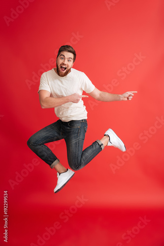 Emotional bearded man jumping pointing to copyspace.
