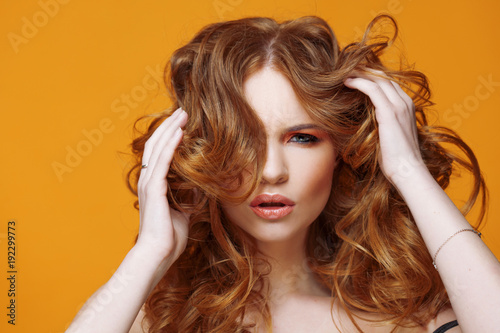Happy redheaded young woman with luxurious curly hair. Studio portrait on yellow background. Excellent hair