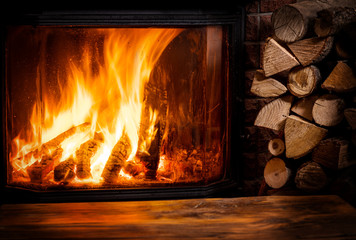Old wooden table and fireplace with warm fire at the background.