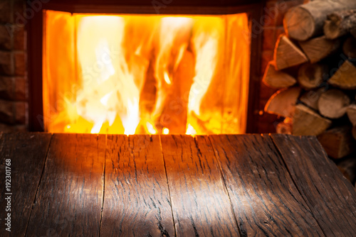 Empty wooden table and fireplace with warm fire at the background.