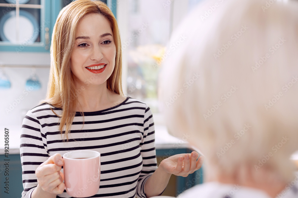 Sharing thoughts. The focus being on a pretty young woman talking to her elderly mother and smiling at her fondly while telling about her day and drinking coffee Sharing thoughts. The focus being on a pretty young woman talking to her elderly mother and smiling at her fondly while telling about her day and drinking coffee