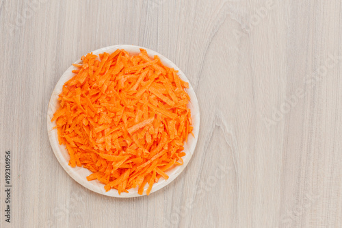 plate of grated carrots on wooden background