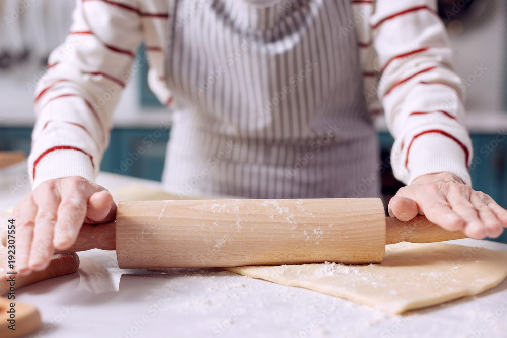 Future pie. The close up of delicate hands of an elderly lady in an apron using a rolling pin to roll out dough while making a pie Future pie. The close up of delicate hands of an elderly lady in an apron using a rolling pin to roll out dough while making a pie