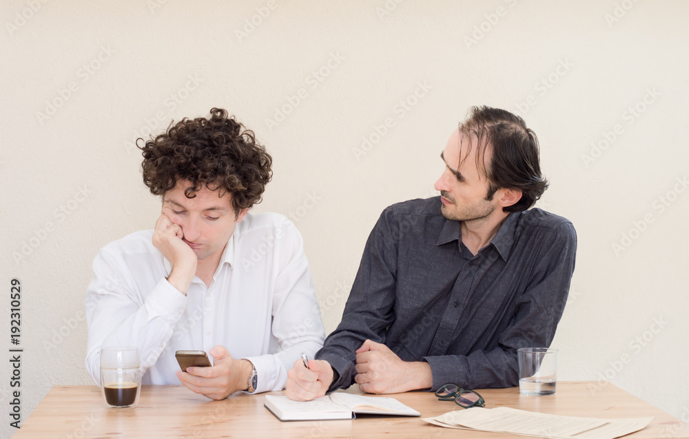 Young Caucasian businessman making a face at his colleague in office with light background.