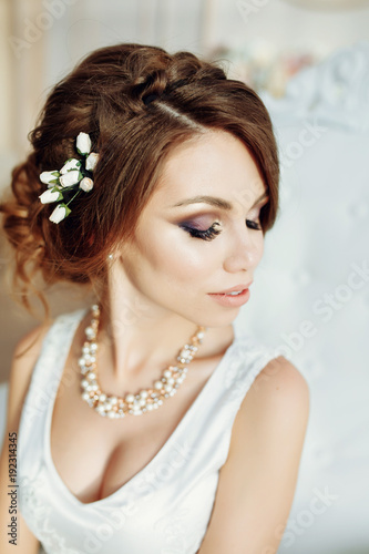 Wedding. Bride in beautiful dress sitting on sofa indoors in white studio interior like at home. Trendy wedding style shot in full length. Young attractive caucasian brunette model like a bride